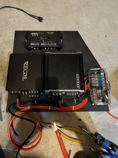 Two car amplifiers on a mounting board with a fuse distribution block and red power cables