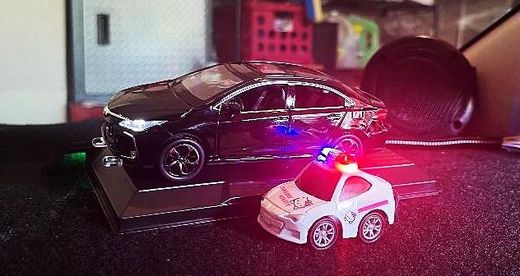 Black model sedan on a display base with its headlights lit